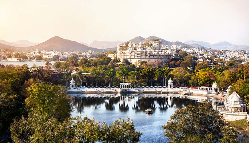 view of the palace on the lake in udaipur with mountains and green surrounding the island in india