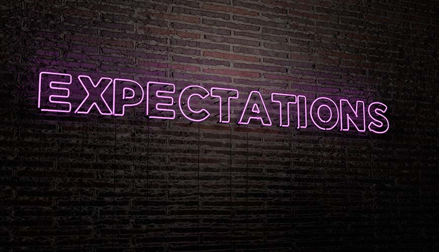 glowing wall light on brick wall saying "expectations" in pink writing