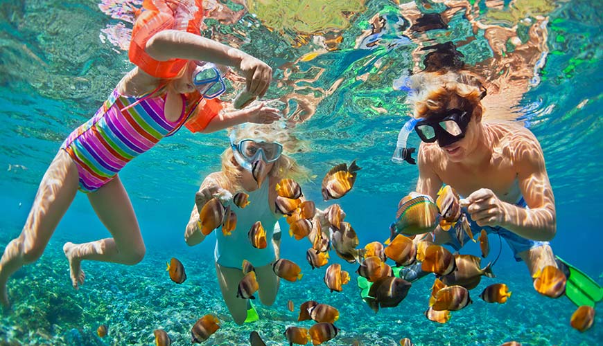 father and his two children snorkelling in crystal blue water, travel experiences for families