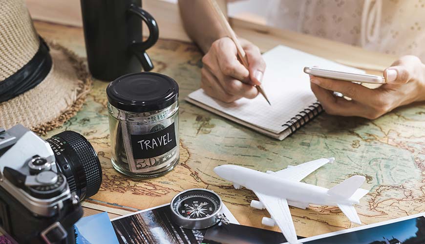 keen budget traveller planning their next holiday surrounded by model plane, world map and travel money jar