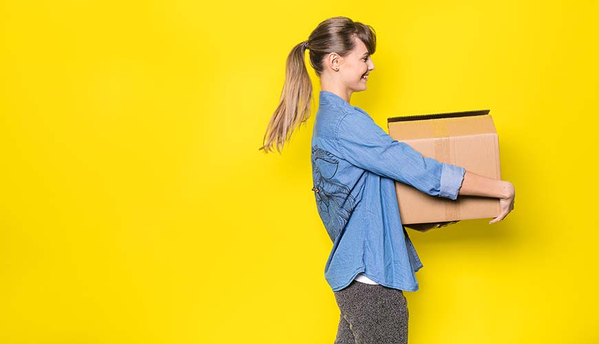 happy woman with moving box walking in front of yellow background
