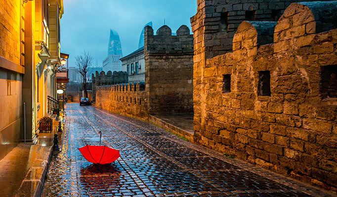 Old city in Baku on a rainy day with red umbrella on the street and the famous flame towers in the background