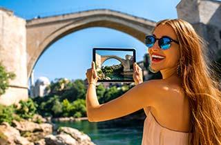 Single woman travelling solo in Eastern Europe, taking a photo of the old bridge in Mostar during summer in Bosnia and Herzegovina