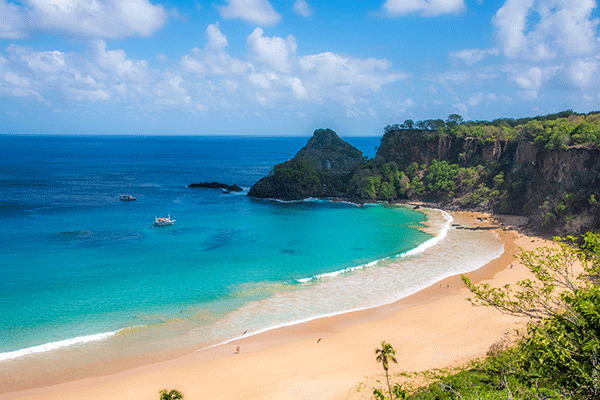 Praia do Sancho - Fernando de Noronha blue sea lining beach with green cliffs behind the beach in Brazil