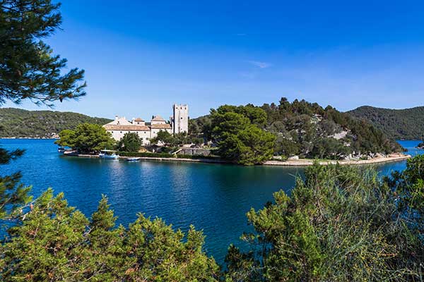 the monastery sitting on the island in Mljet national park in croatia with a clear blue sky and lake surrounding it