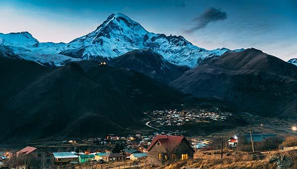 stepantsminda town lit up at night under hills valleys with mount kazbek in the background