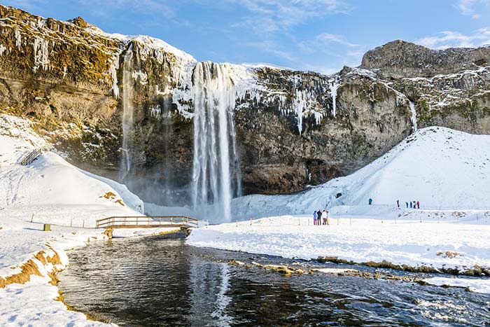 Frozen waterdall seljalandsfoss waterfall under the sunrise lights in winter reflection in river iceland tours