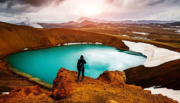 Tour to Iceland, Lake Myvtan solo traveller on group tour to iceland standing over the blue lake myvtan with hills and steam and snow surounding