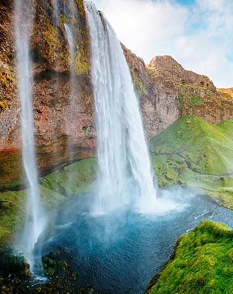 Seljalandsfoss Waterfall in summer in Iceland cascading waterfall into blue pool below with green grass and high rocks on a trip to iceland