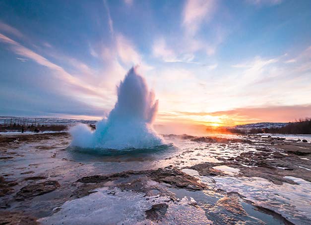 strokkur geysir erupting with a sunset in the background in iceland