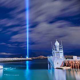 Imagine Peace Tower, Iceland boats moored on lake with beam of blue light from imagine peace tower