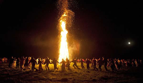 Summer Solstice, Iceland people holding hands dancing in a circle around a bonfire for summer solstice in iceland