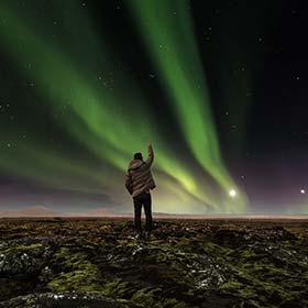 Aurora Borealis - The nothern lights, Iceland solo traveller standing with arm pointed to the sky showing northern lights aurora