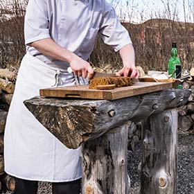 Culture Night, Iceland Man making traditional dark rye bread in iceland with white apron slicing bread on tree trunk