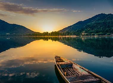 small boat on calm lake in srinagar kashmir in india with green mountain hills in the background