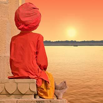 indian man wearing an orange turban and traditional indian dress looking over the lake towards the sunset