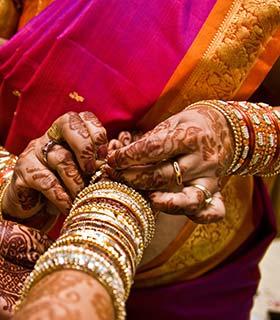 close up of an indian woman decorating another indian womans hands for her wedding with bangles bracelets and henna