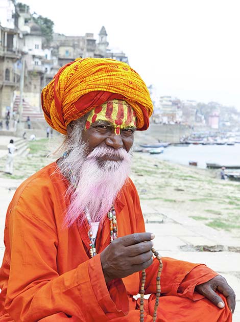 holy sadhu man in india sitting beside the holy river ganges in varanasi wearing bright clothes and facepaints with a pink beard