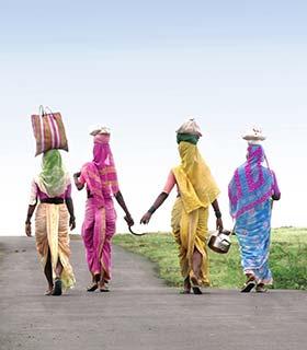 group of indian women carrying pots and bags on their heads wearing colourful traditional indian clothing of saris