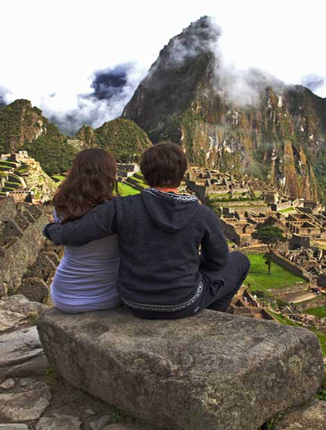 Adventure travel couple sit overlooking Machu Picchu ruins Couple of adventure travellers look in awe of their surroundings as they sit overlooking acient Machu Picchu ruins
