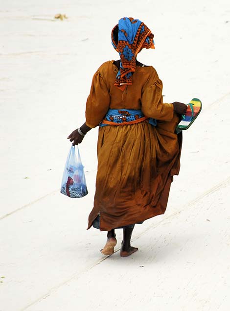 Tanzanian Woman in traditional dress in Zanzibar traditionally dressed tanzanian woman walking on the beach in zanzibar