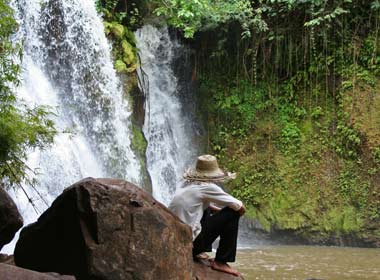 Man sits at waterfall along the ekong trail in Kratie on holiday in Cambodia on tour