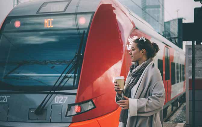 female traveller getting around europe by train standing with coffee by red train in station
