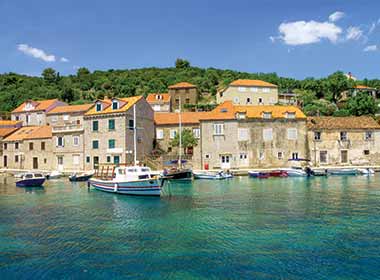 turqoise water with boats floating near a line of brick houses on sipan island croatia