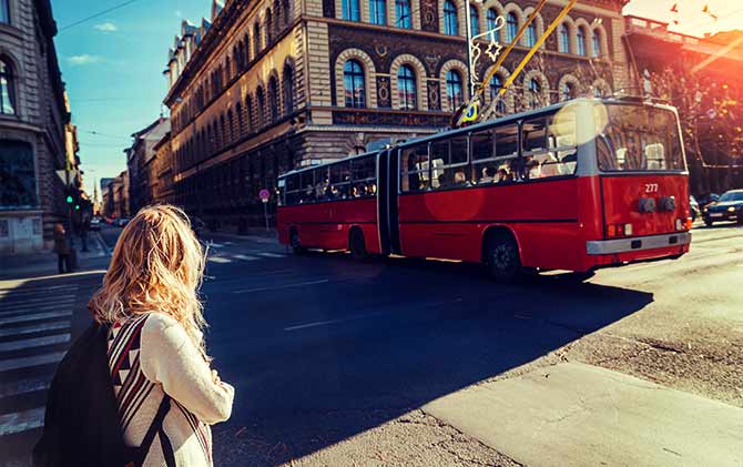 Solo woman travelling in Europe using a red bus crossing the road