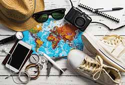 What to pack on a solo holiday to Europe. A table of accessories including shoes, plimsoles, sunglasses, hat, iphone, bracellets, watch, camera, notebook and pen lying on a white wooden table