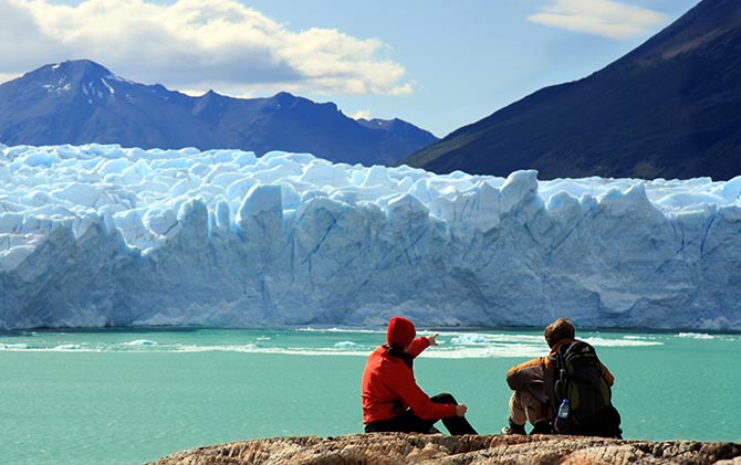 Couple sitting at Perito Moreno glacier, Southern Patagonian Ice Field, El Calafate, Argentina Sky, glacier and rocks:Glacier Perito Moreno, Southern Patagonian Ice Field, El Calafate, Argentina