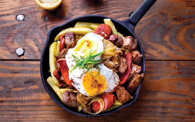 Chilean food, chorrillana - french fries, beef sliced, sausages chorrisos, fried onion and eggs served in cast iron pan with sauces 