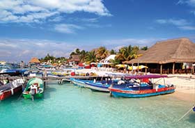 Highlights of Mexico group tour Fishing boats on the beach and turqoise sea with wooden huts on the beach in Mexico