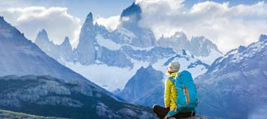 Adventure holiday traveller in patagonia on a hiking trail sits to admire the view of mount fitz roy between chile & argentina 