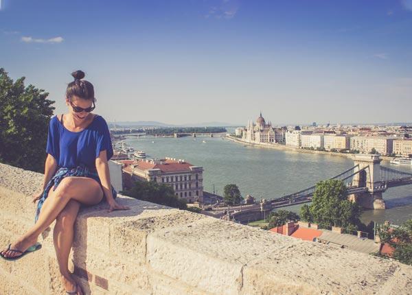 Female single tourist traveller with Tucan Travel on her trip happily posing infront of the Budapest skyline single traveler in awe of her surroundings an amazing background of the Danube River and Budapest skyline in Hungary