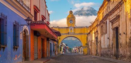 Antigua City at sunrise with the famous yellow arch in the center and the active Agua volcano Guatemala on her singles trip with Tucan Travel solo tourist exploring Antigua, Guatemala