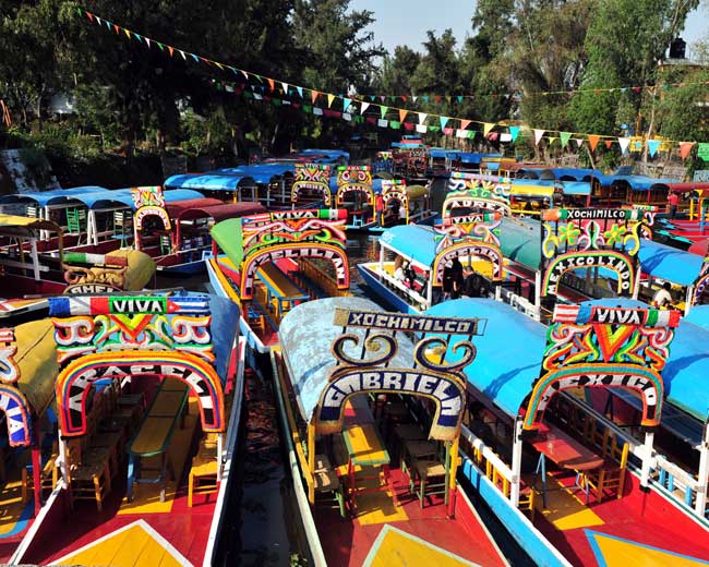 tourists on holiday travel on the colourful mexican gondolas at xochimilcos floating gardens in the canals of mexico city