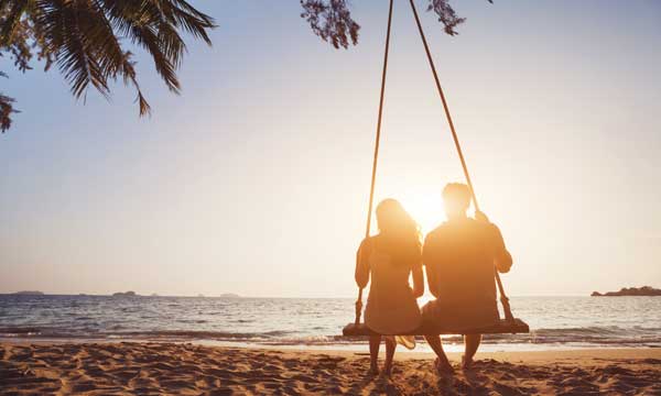 Romantic couple share a swing on a tropical beach in sri lanka experienceing a moment together whilst on holiday